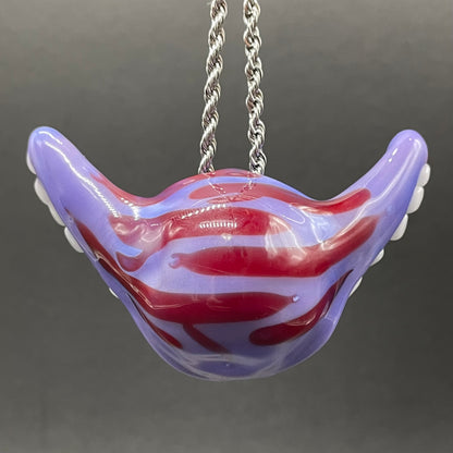 A novelty mouth-shaped pendant necklace made of glossy purple and red glass with white teeth details, suspended from a silver chain against a dark gray background.
