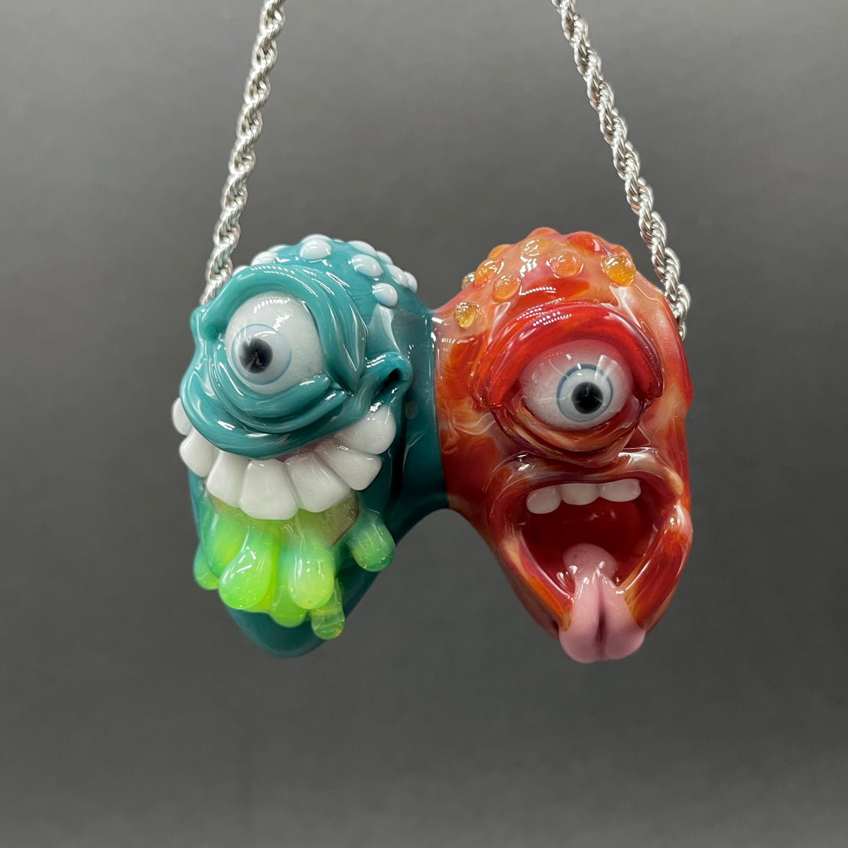 Two Headaches Are Better Than One handblown glass pendant - teal cyclops head with white teeth and green slime fused with red cyclops head with pink tongue, silver rope chain - Leviathan Glass