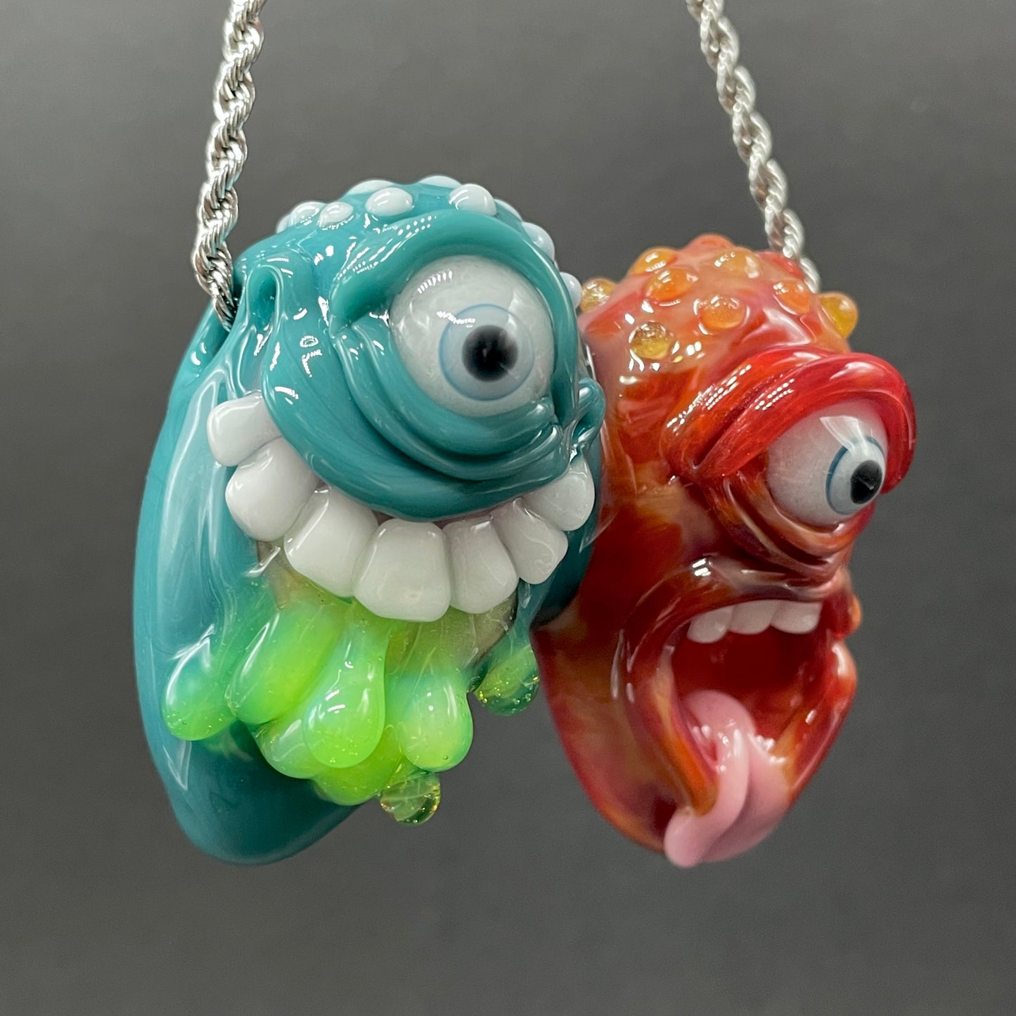 Two Headaches Are Better Than One handblown glass pendant - teal cyclops head with white teeth and green slime fused with red cyclops head with pink tongue, silver rope chain - Leviathan Glass