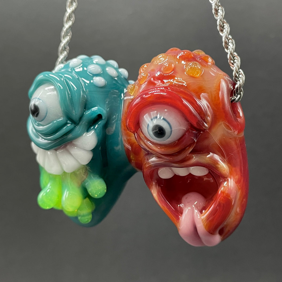 Two Headaches Are Better Than One handblown glass pendant - teal cyclops head with white teeth and green slime fused with red cyclops head with pink tongue, silver rope chain - Leviathan Glass