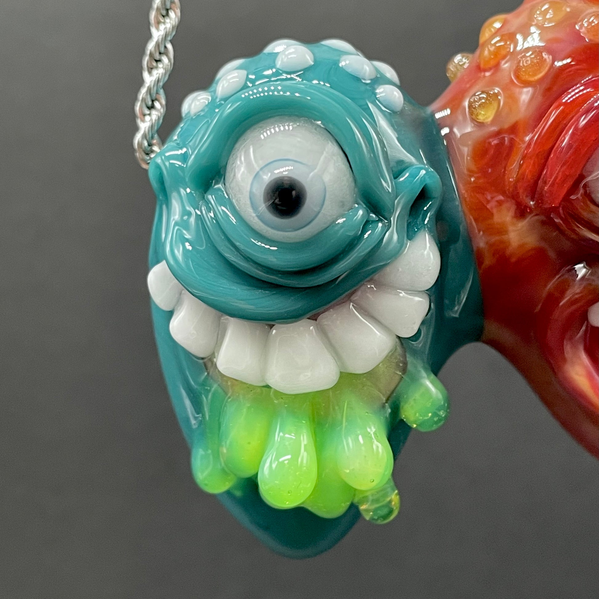 Two Headaches Are Better Than One handblown glass pendant - teal cyclops head with white teeth and green slime fused with red cyclops head with pink tongue, silver rope chain - Leviathan Glass