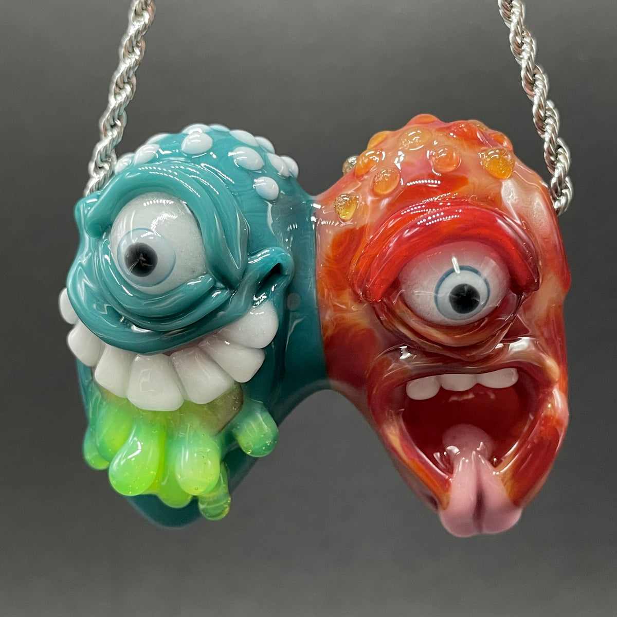 Two Headaches Are Better Than One handblown glass pendant - teal cyclops head with white teeth and green slime fused with red cyclops head with pink tongue, silver rope chain - Leviathan Glass