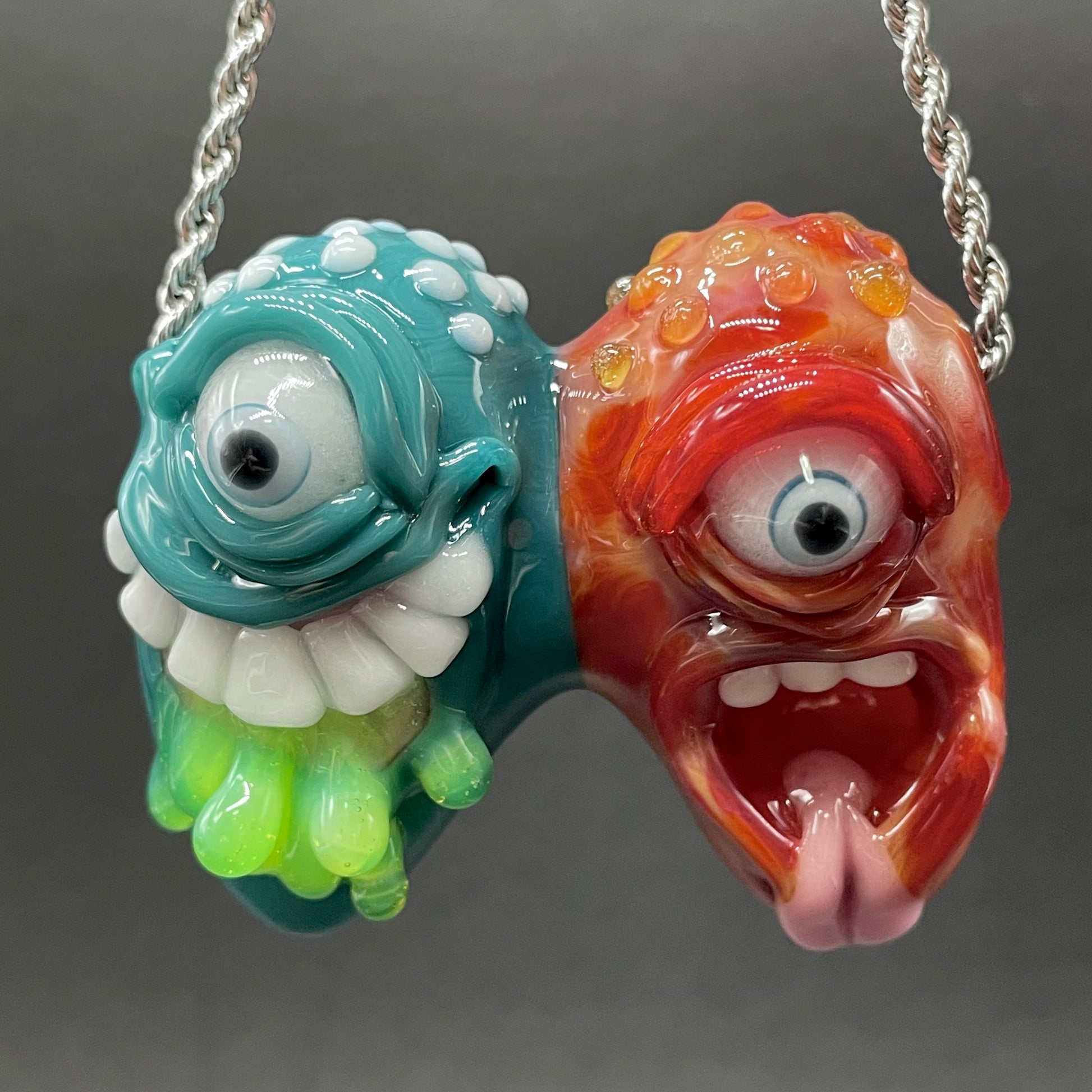 Two Headaches Are Better Than One handblown glass pendant - teal cyclops head with white teeth and green slime fused with red cyclops head with pink tongue, silver rope chain - Leviathan Glass