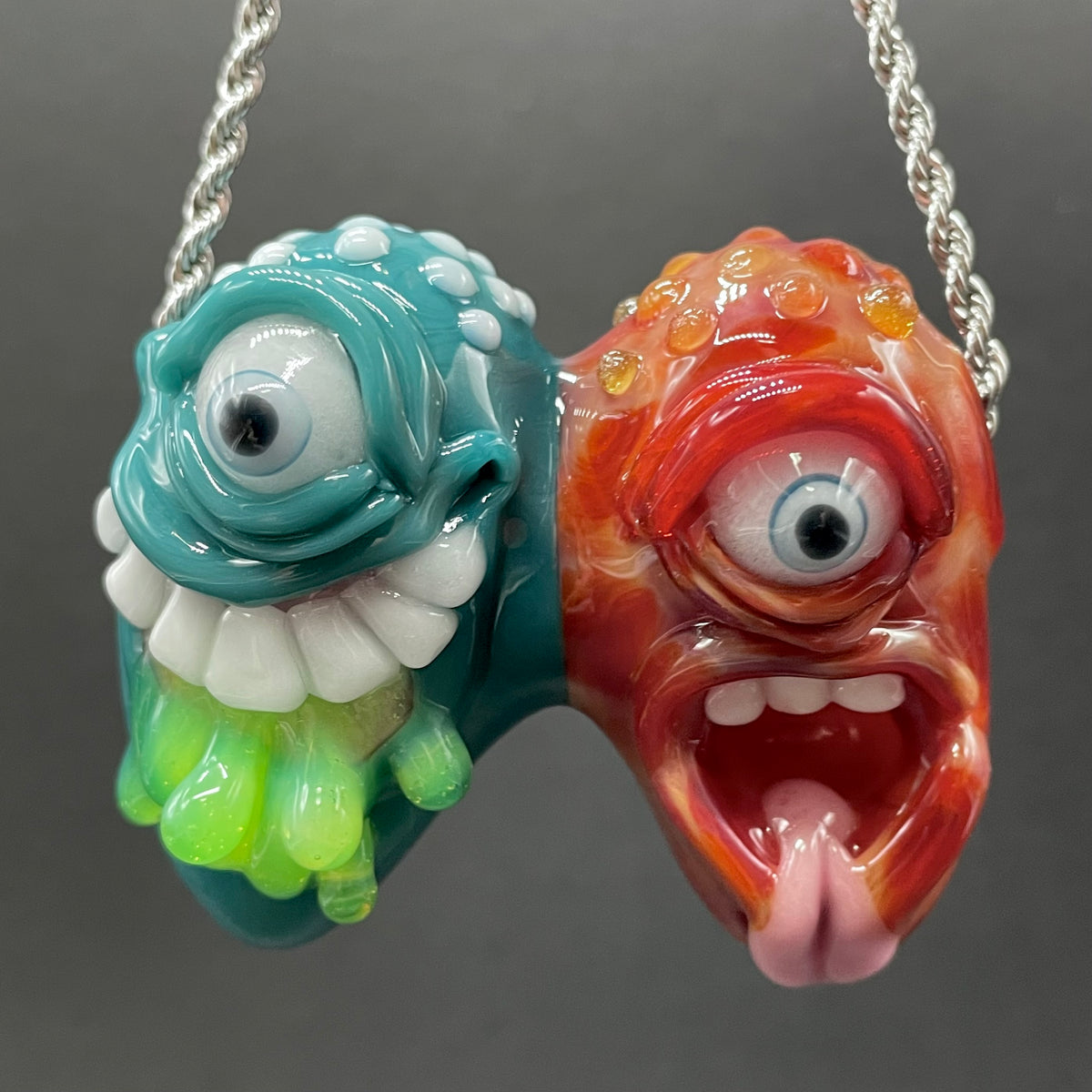 Two Headaches Are Better Than One handblown glass pendant - teal cyclops head with white teeth and green slime fused with red cyclops head with pink tongue, silver rope chain - Leviathan Glass
