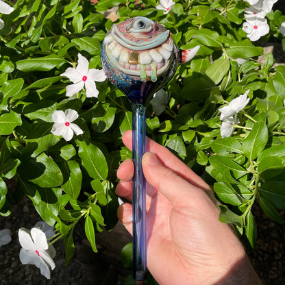 Hand Blown Glass Monster Watering Globe - round cyclops head, blue iris eye, white teeth, gold tooth, teal tongue drips, teal glass stake - Leviathan Glass